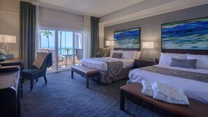 A hotel room with a large bed, a smaller bed, a desk, and a chair. There is a balcony with a view of the ocean. - Tamarack Beach Resort Hotel (Carlsbad)