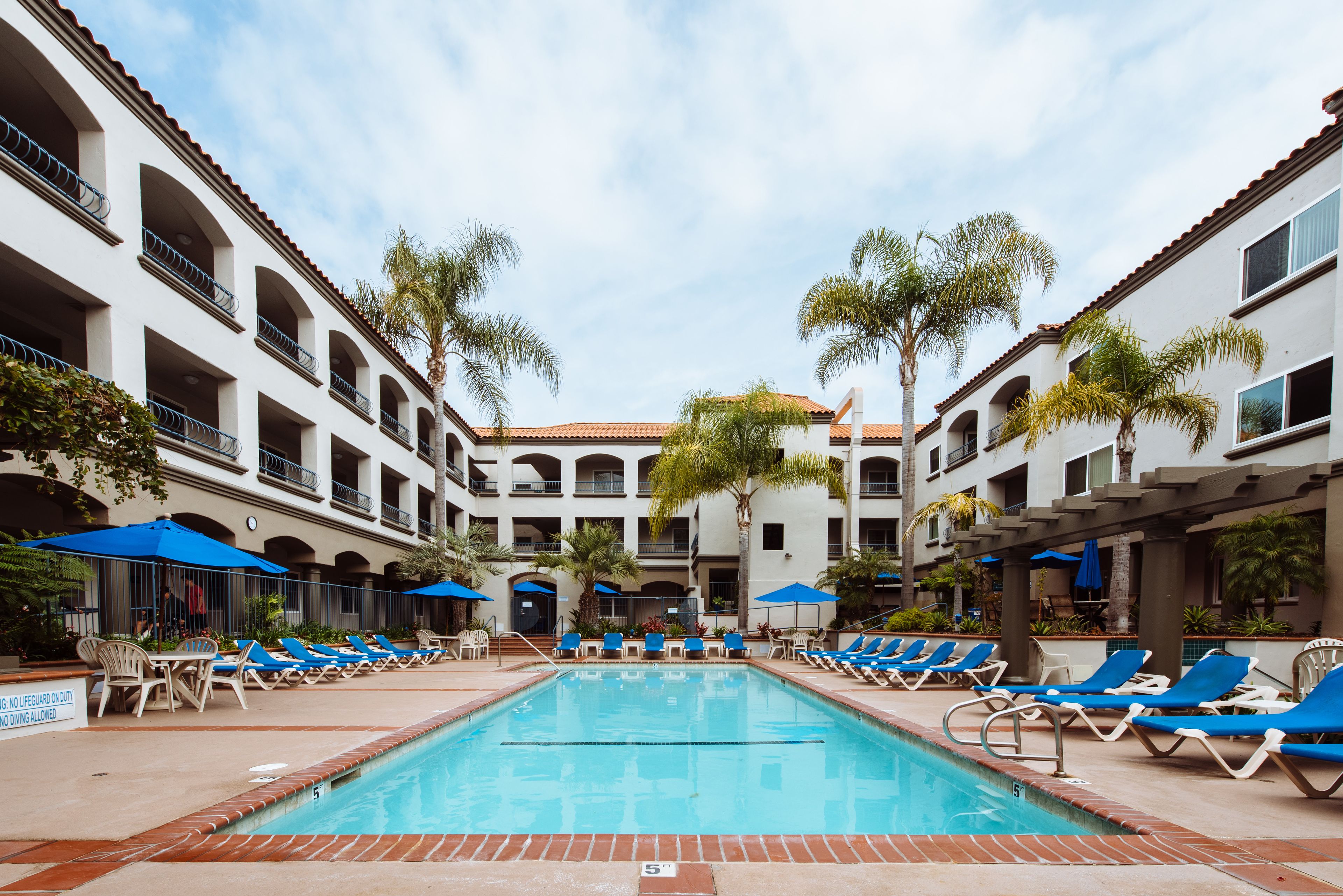 A pool area with lounge chairs and umbrellas, surrounded by multi-story buildings with balconies.