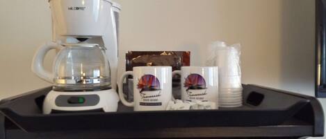 En kaffebryggare, två muggar med tryck och en hög med engångsmuggar på ett bricka.