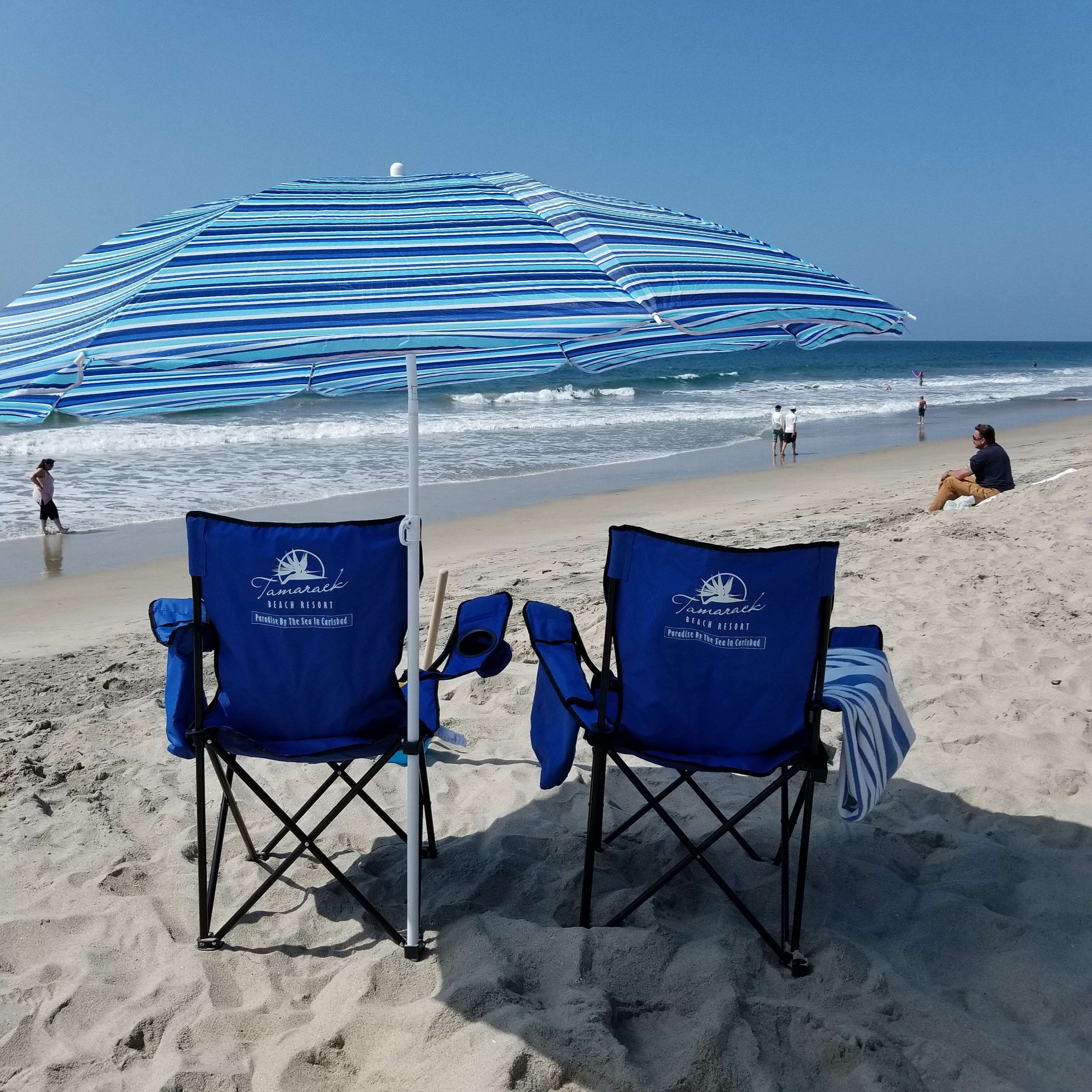 Two beach chairs with a blue and white striped umbrella, a sandy beach, and the ocean in the background.