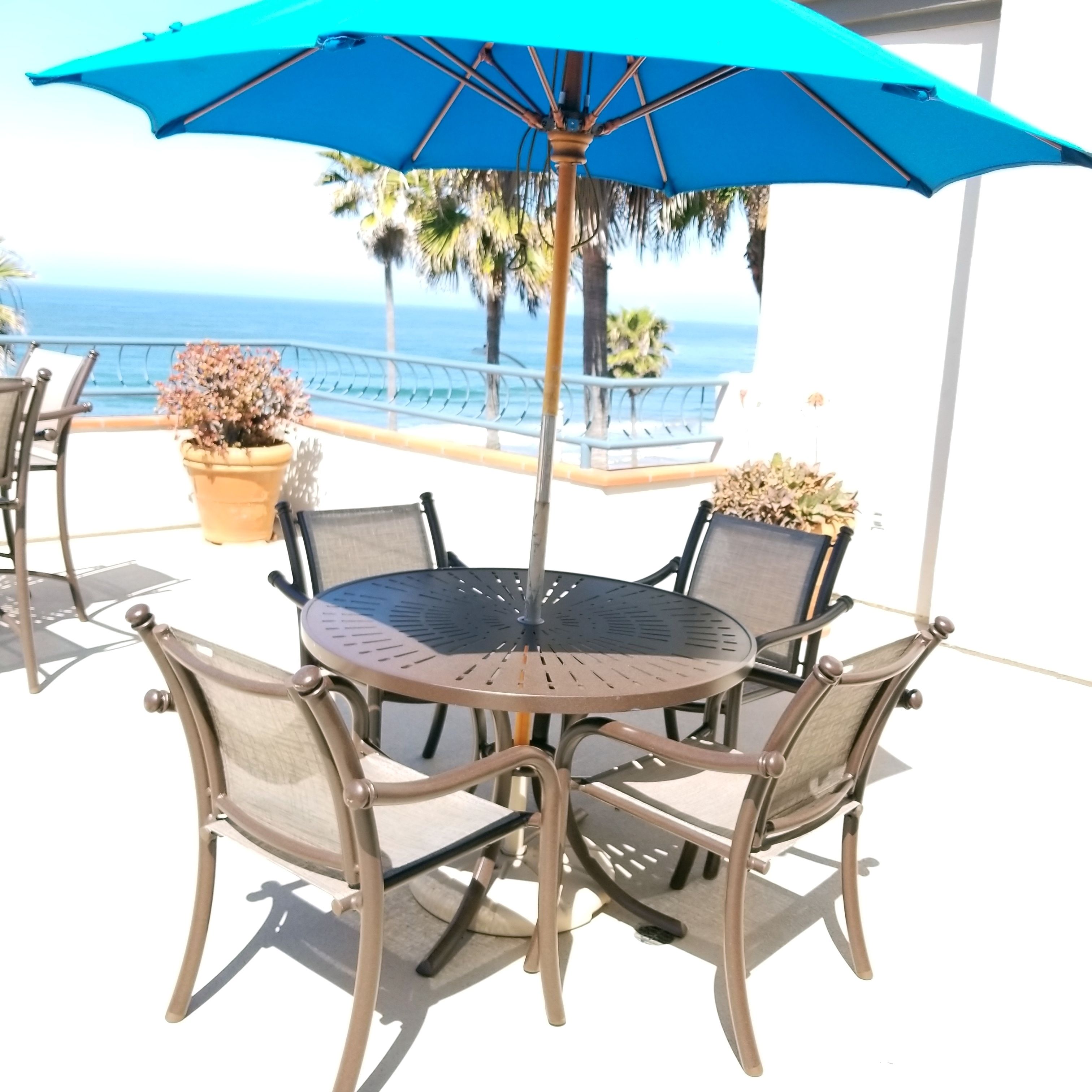 A round metal table with four chairs and a blue umbrella.