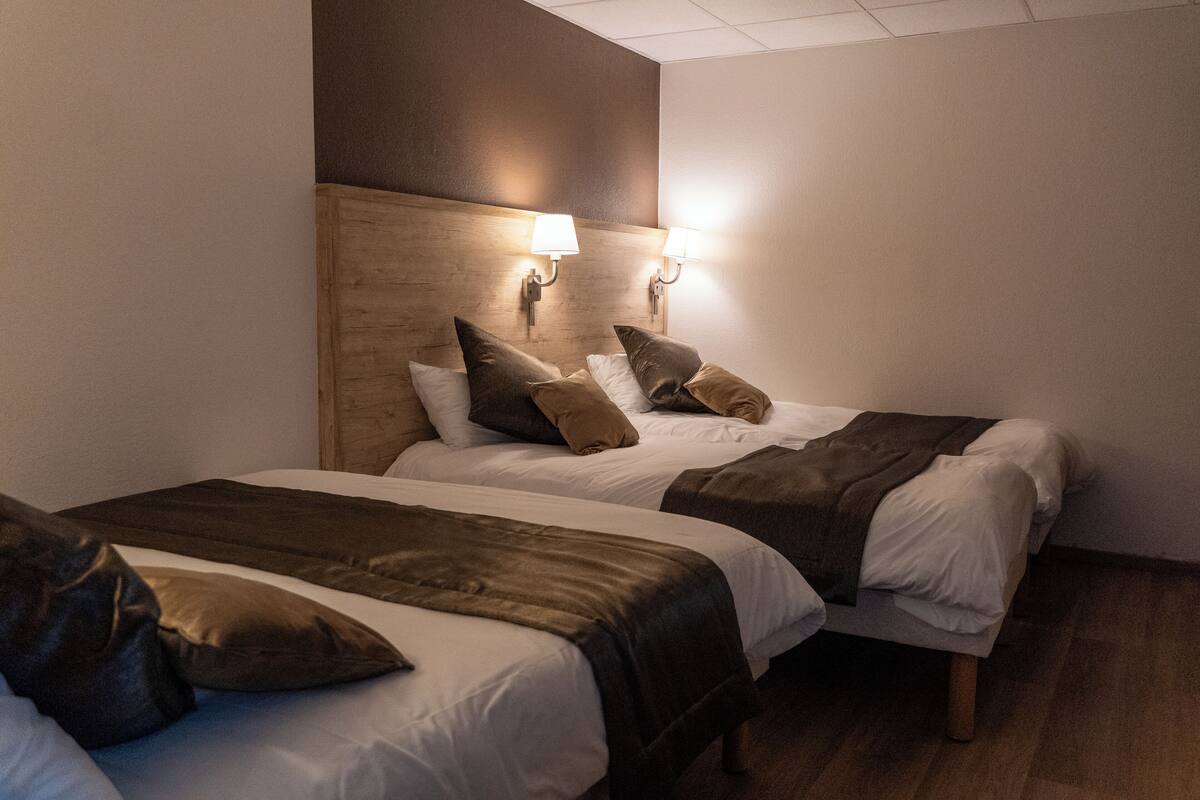 Ein Hotelzimmer mit zwei Betten, einem Holzkopfstück und Wandlampen.