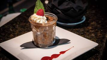 Un postre en un vaso transparente sobre un plato blanco, con un goteo de salsa roja, sobre una encimera de granito oscuro.