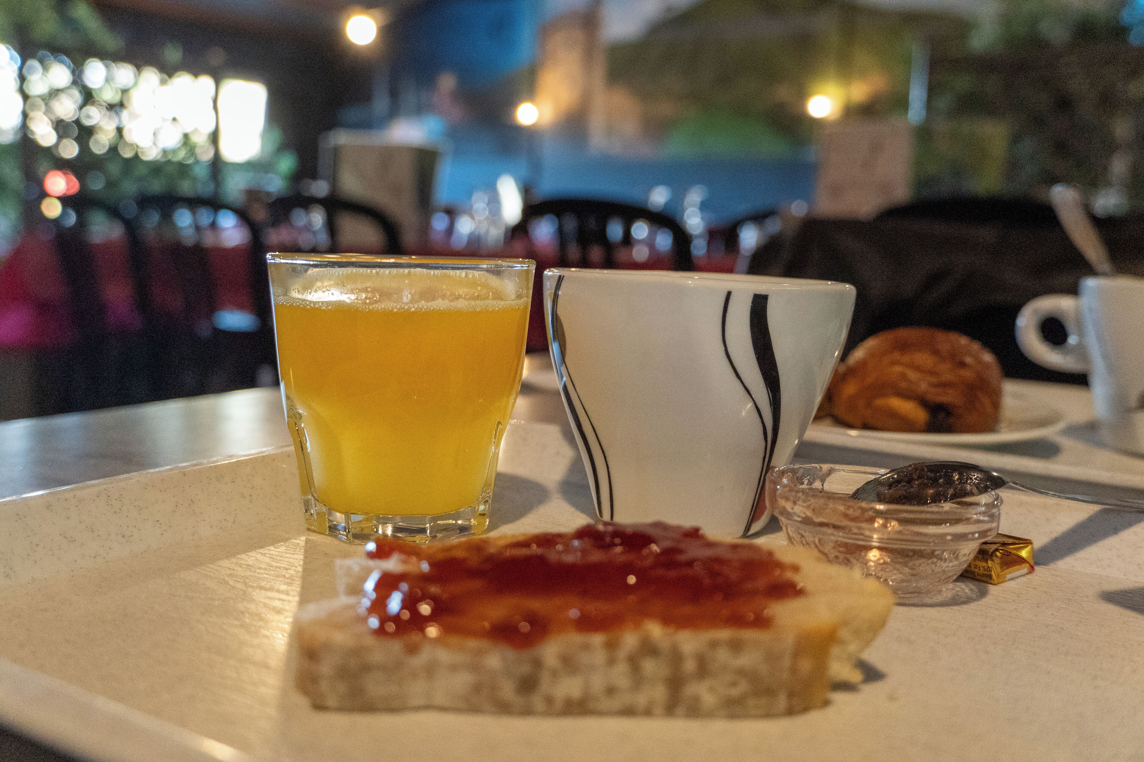 Ein Frühstücksarrangement mit Orangensaftglas, weißer Tasse, einem Croissant und einer kleinen Schale Marmelade auf einem Tablett.
