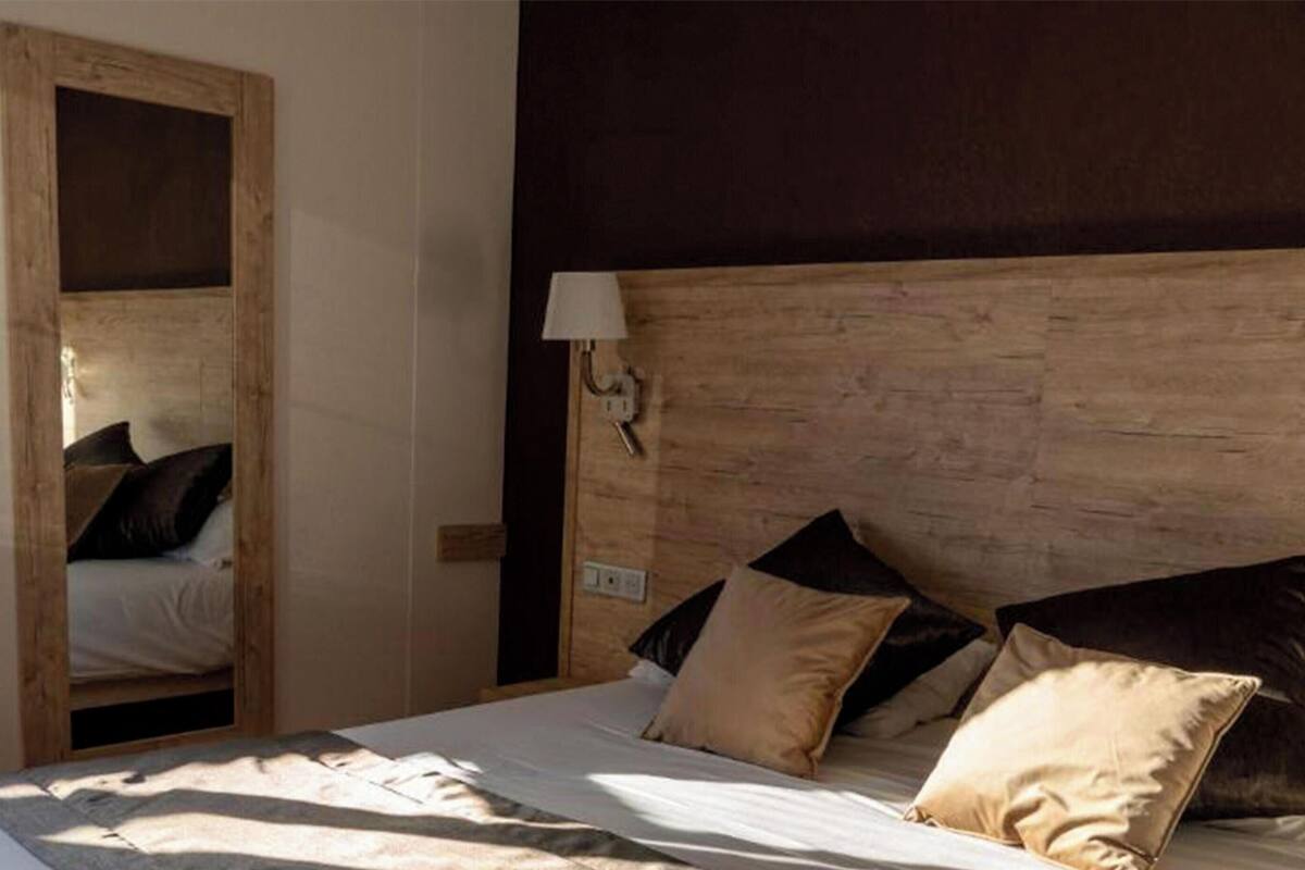 Ein Schlafzimmer mit hölzernem Kopfteil, einem Bett mit vielen Kissen, einem Nachttisch und einem Spiegel.
