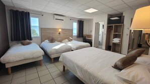 Une chambre d’hôtel avec trois lits, un bureau, une armoire et une salle de bain visible à travers une porte ouverte.