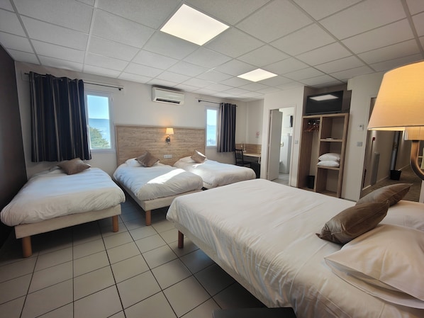 A hotel room with three beds, a desk, a wardrobe, and a bathroom visible through an open door.