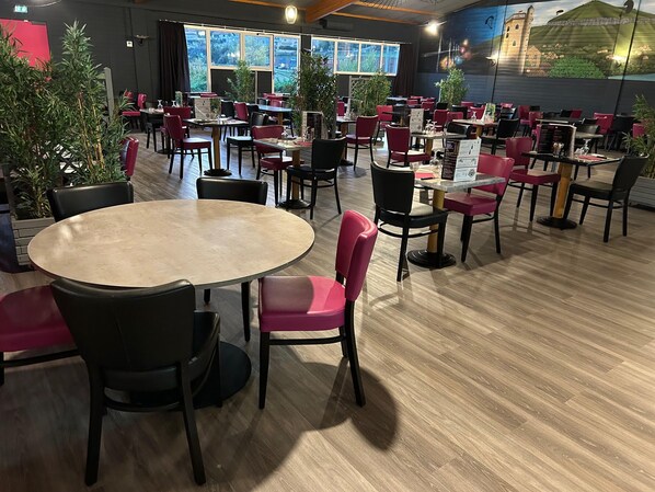Un restaurante con varias mesas y sillas, suelo de madera y grandes ventanales con vistas al exterior.