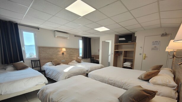 A hotel room with four beds, a wooden headboard, a TV, a wardrobe, and a window with curtains. - Cit'Hotel Restaurant Bowling de Millau (Millau)
