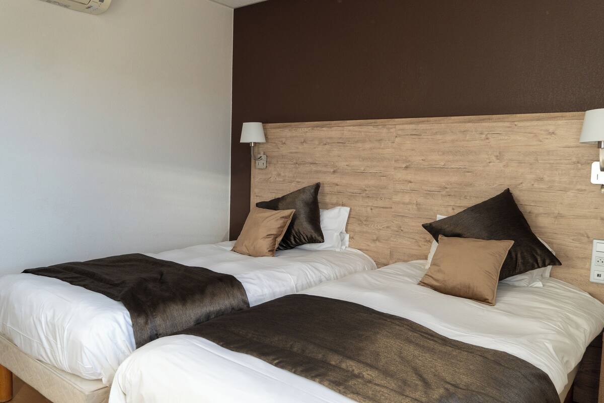 Ein Hotelzimmer mit zwei Betten, jeweils mit einem hölzernen Kopfteil, weißer Bettwäsche und braunen Zudecken.