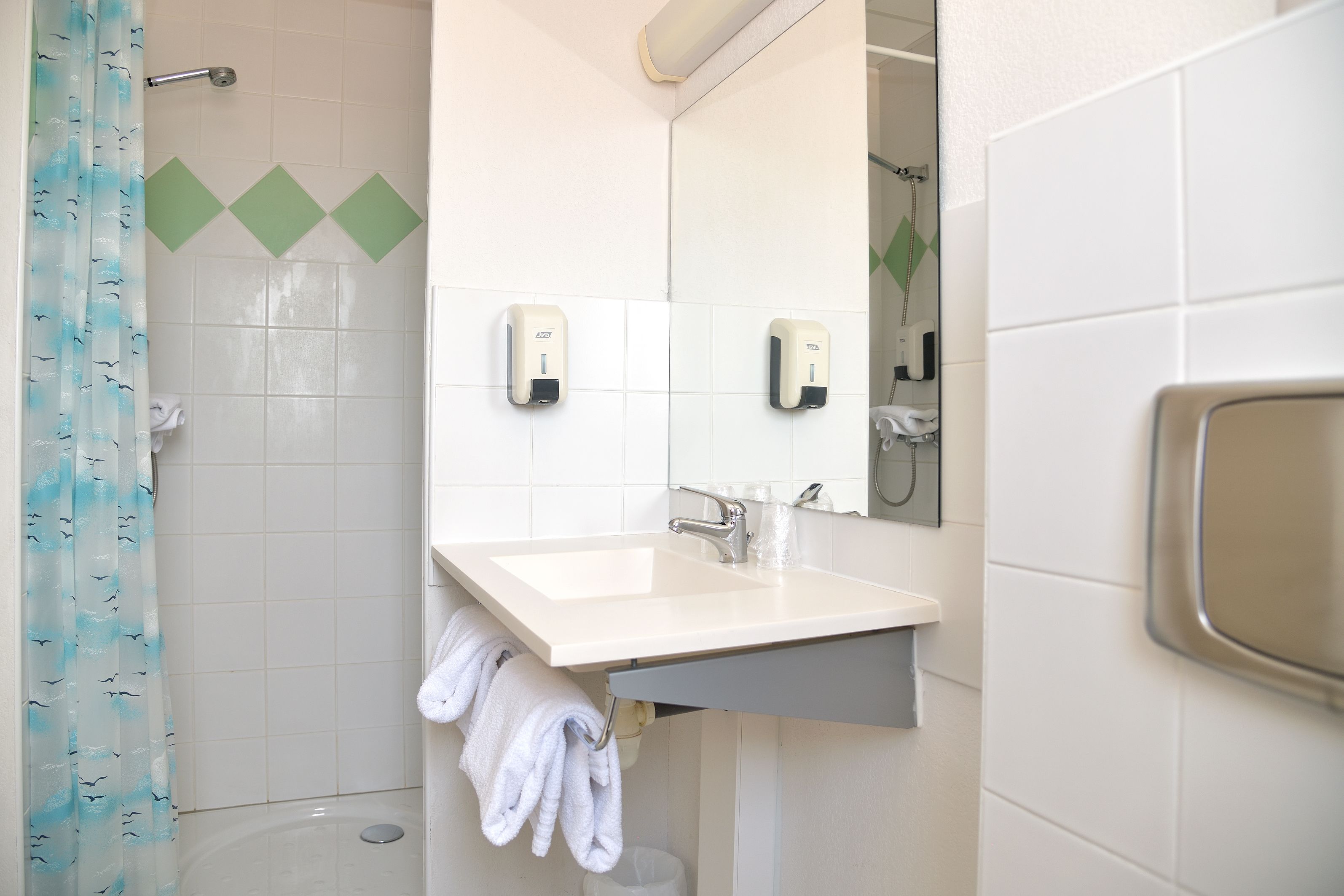 Un baño con un lavamanos blanco, dos dispensadores de jabón, un espejo y una cortina de ducha.