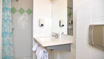 Un baño con un lavamanos blanco, dos dispensadores de jabón, un espejo y una cortina de ducha.
