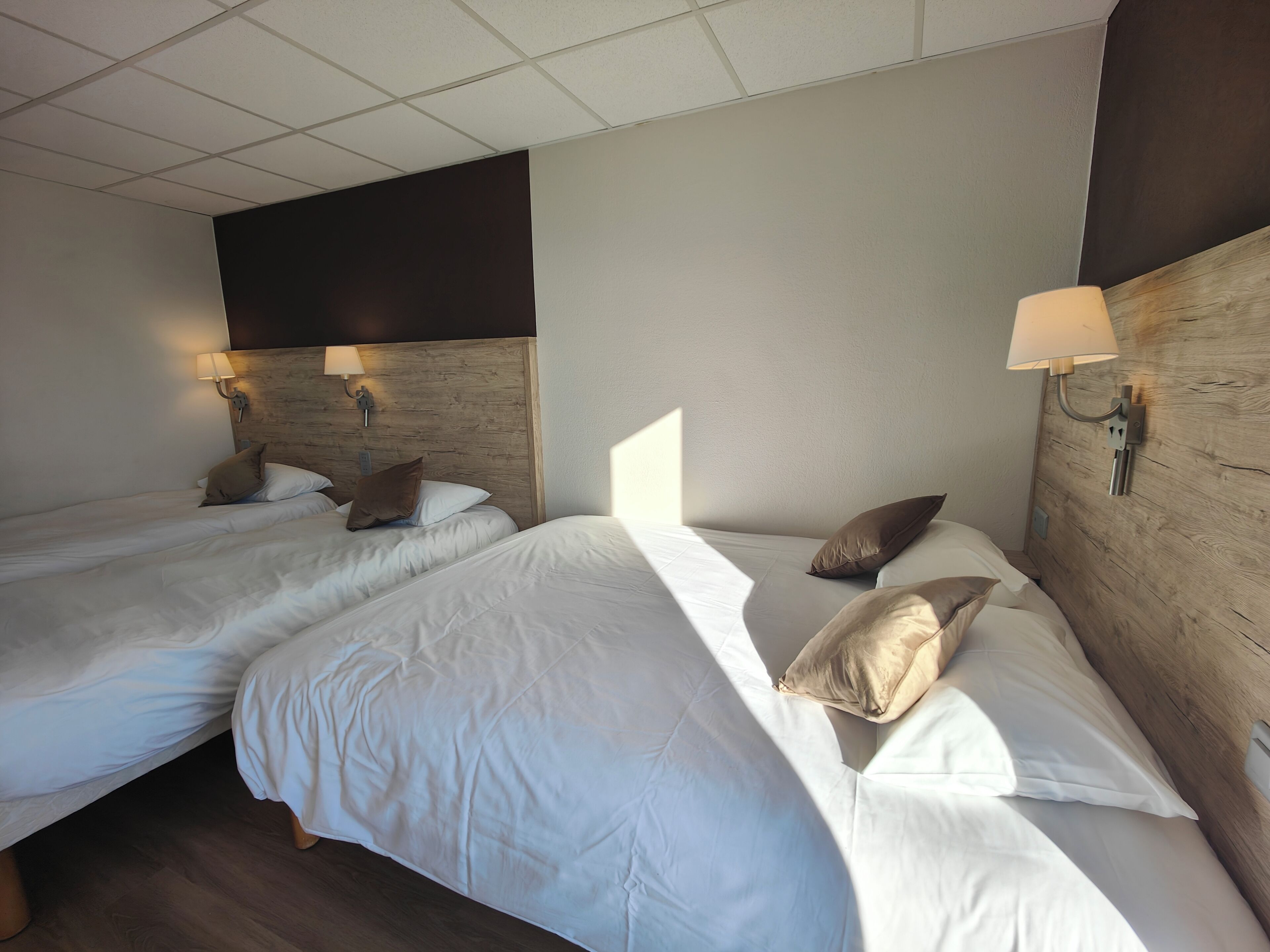 Una camera d'albergo con due letti singoli, ognuno con biancheria bianca e un poggiatesta in legno. Ai lati dei letti sono presenti lampade fissate alla parete.