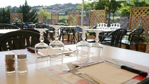 Un espace de restauration en plein air avec des tables préparées pour deux personnes, comprenant couverts, salière et poivrière, ainsi que des verres à vin.