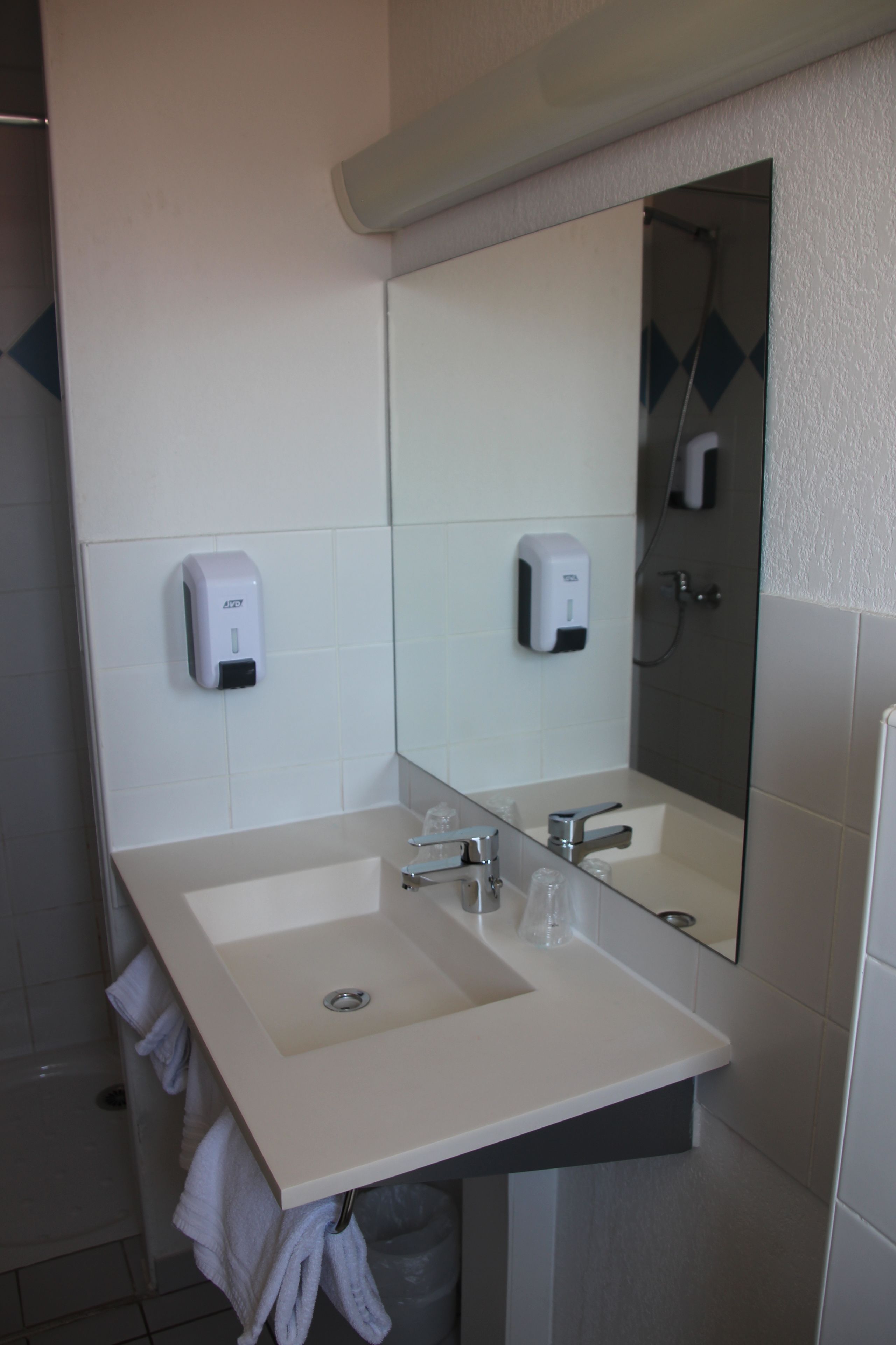 A bathroom with a white sink, two soap dispensers, a mirror, and a shower area.