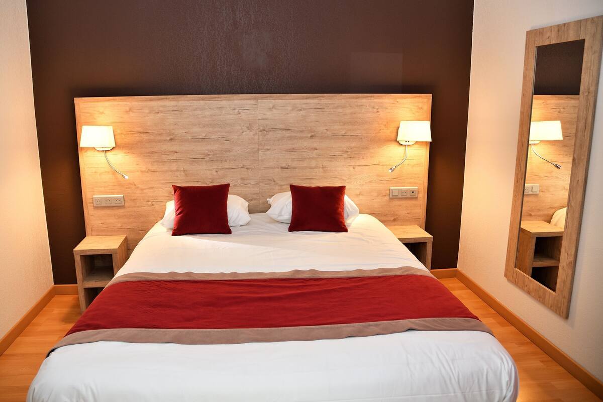 Ein Hotelzimmer mit einem großen Bett, zwei Nachttischen, einem Holzkopfende und einem Spiegel an der Wand.
