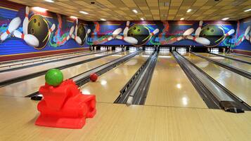 A bowling alley with multiple lanes, colorful murals, and a red bowling ball on the floor.