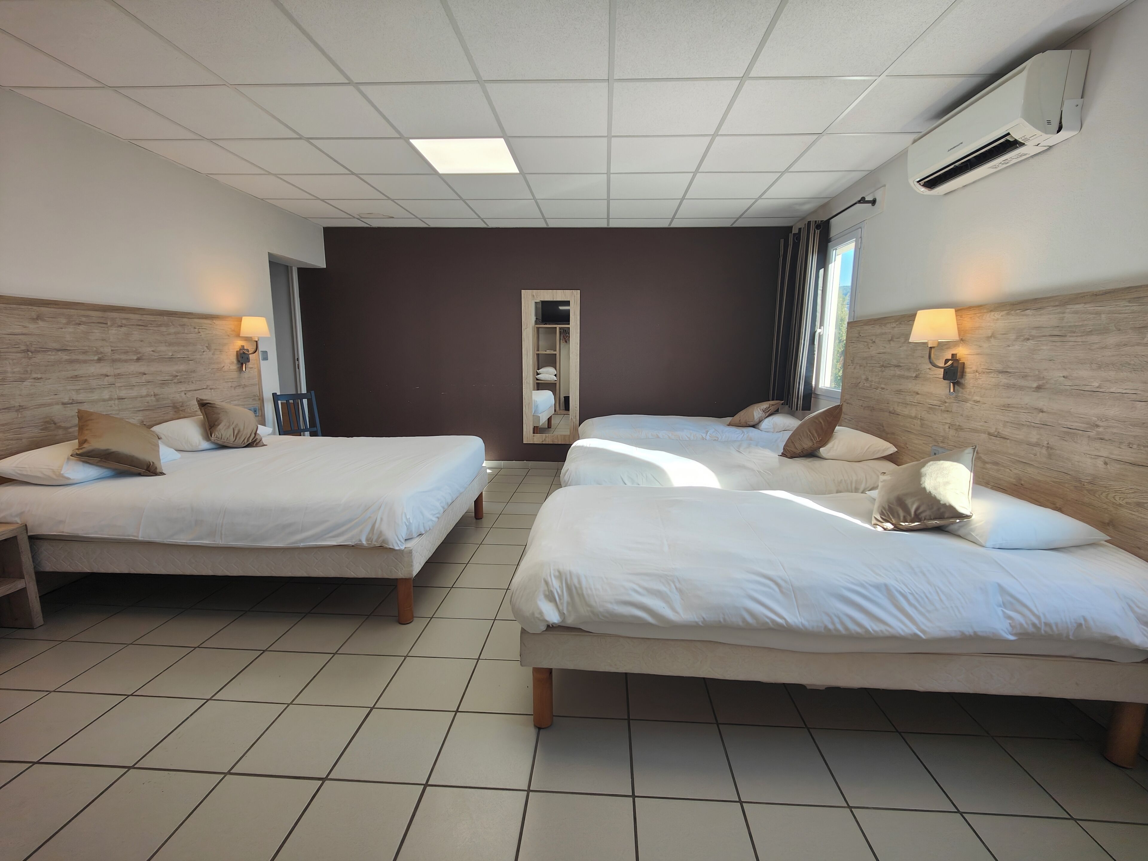 A hotel room with two beds, a wooden headboard, a mirror, and an air conditioning unit.