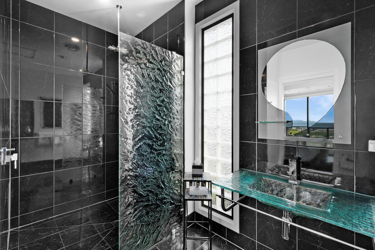 A modern bathroom with a glass shower enclosure, a large mirror, and a view of the outdoors.