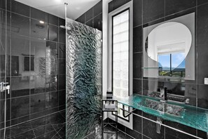 Un baño moderno con cabina de ducha de vidrio, un espejo grande y vistas al exterior.