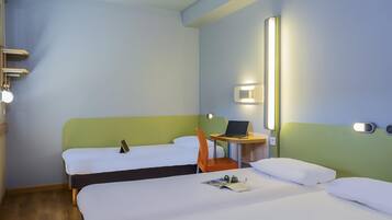 Ett hotellrum med två sängar, ett skrivbord med en bärbar dator, en stol, ett nattduksbord och en väggmonterad lampa.