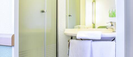 A bathroom with a glass shower door, a sink with a mirror, and two towels.