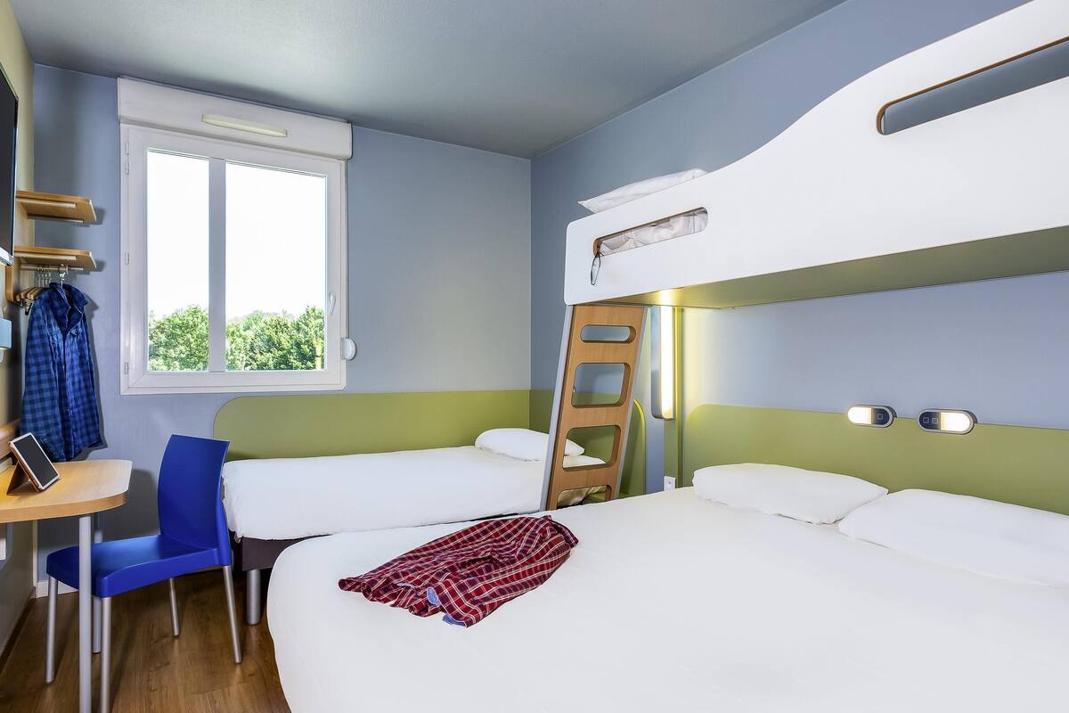 Una habitación con dos camas, un escritorio, una silla, una ventana y una escalera.