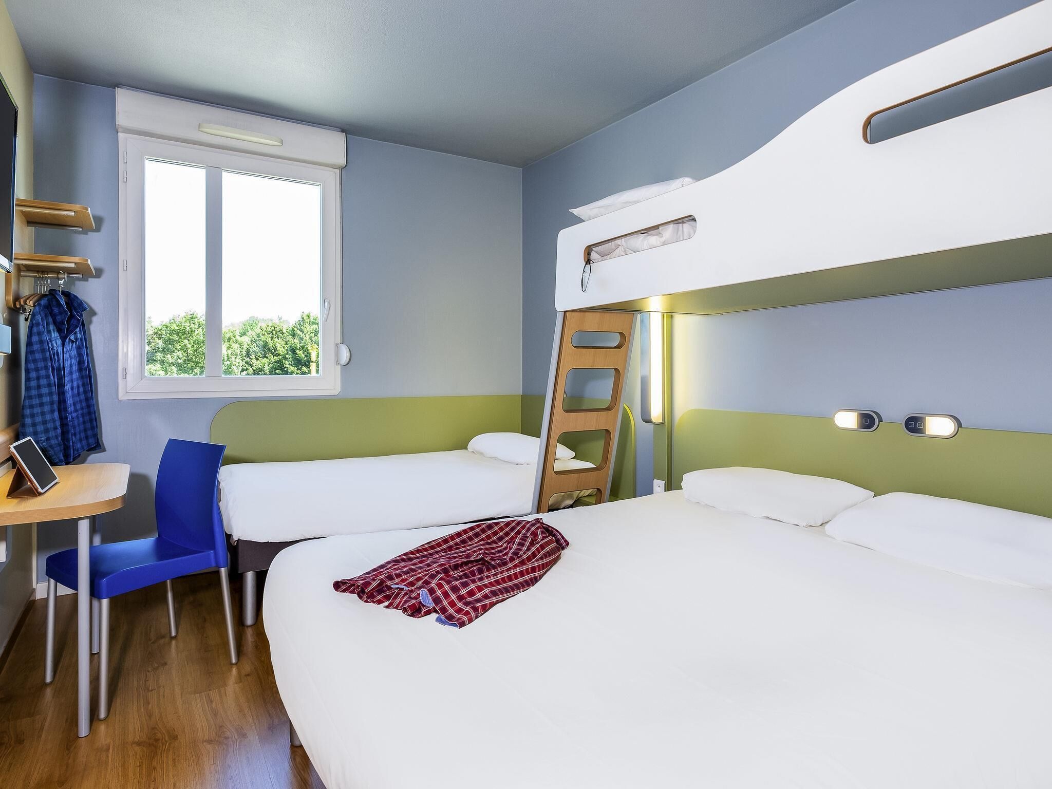 Una habitación con literas, un escritorio con silla, una ventana y una escalera.
