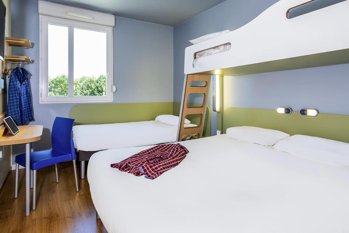 A room with bunk beds, a desk with a chair, a window, and a ladder.