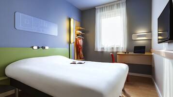 A hotel room with a bed, a desk with a laptop, a TV, and a window with curtains.