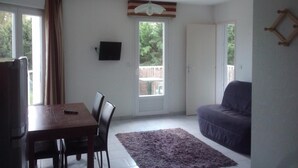 Una habitación con una mesa de comedor, sillas, un sofá morado, un televisor montado en la pared y una puerta que da al exterior.