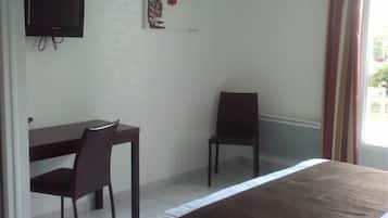 A hotel room with a bed, a desk, two chairs, a television, and a window with curtains.