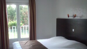 Un dormitorio con cama, ventilador de techo, ventana con cortinas y vista a zonas verdes.