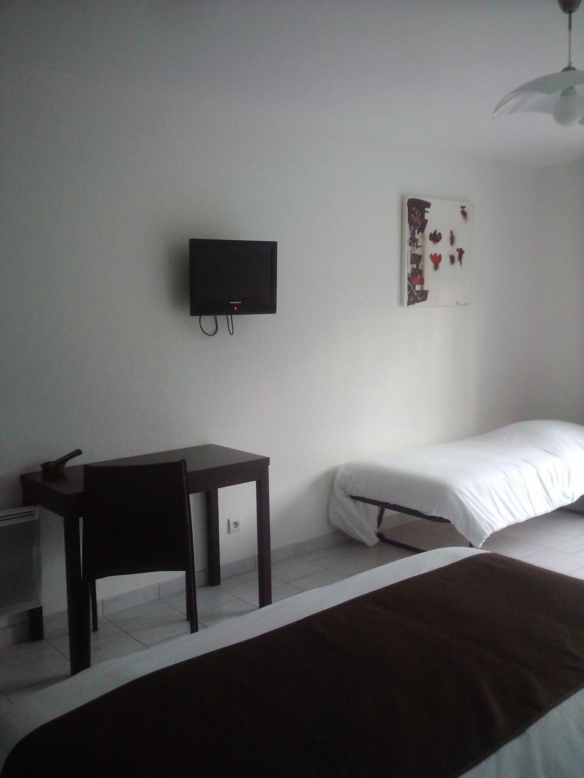 Een slaapkamer met een bed, een bureau, een stoel, een televisie en een kunstwerk aan de muur.