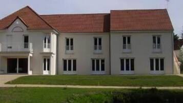 Une maison à deux étages, avec un toit recouvert de tuiles rouges, de nombreuses fenêtres et un porche à l’avant.