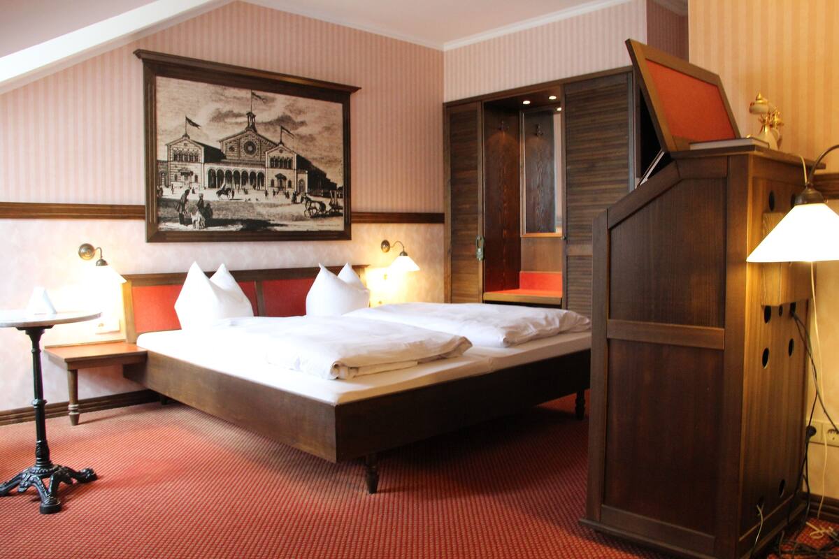 A hotel room with a large bed, two bedside tables with lamps, a wooden wardrobe, and a framed picture on the wall.