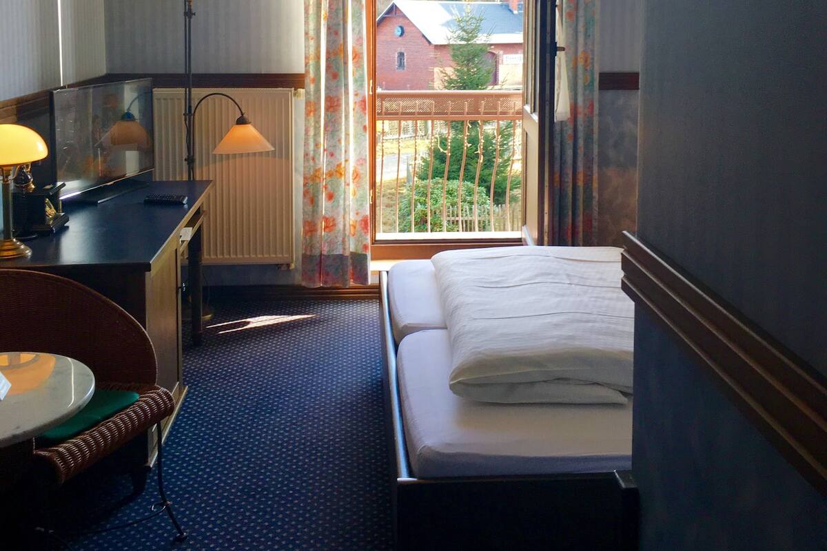 A hotel room with a bed, desk, chair, and a window with curtains.