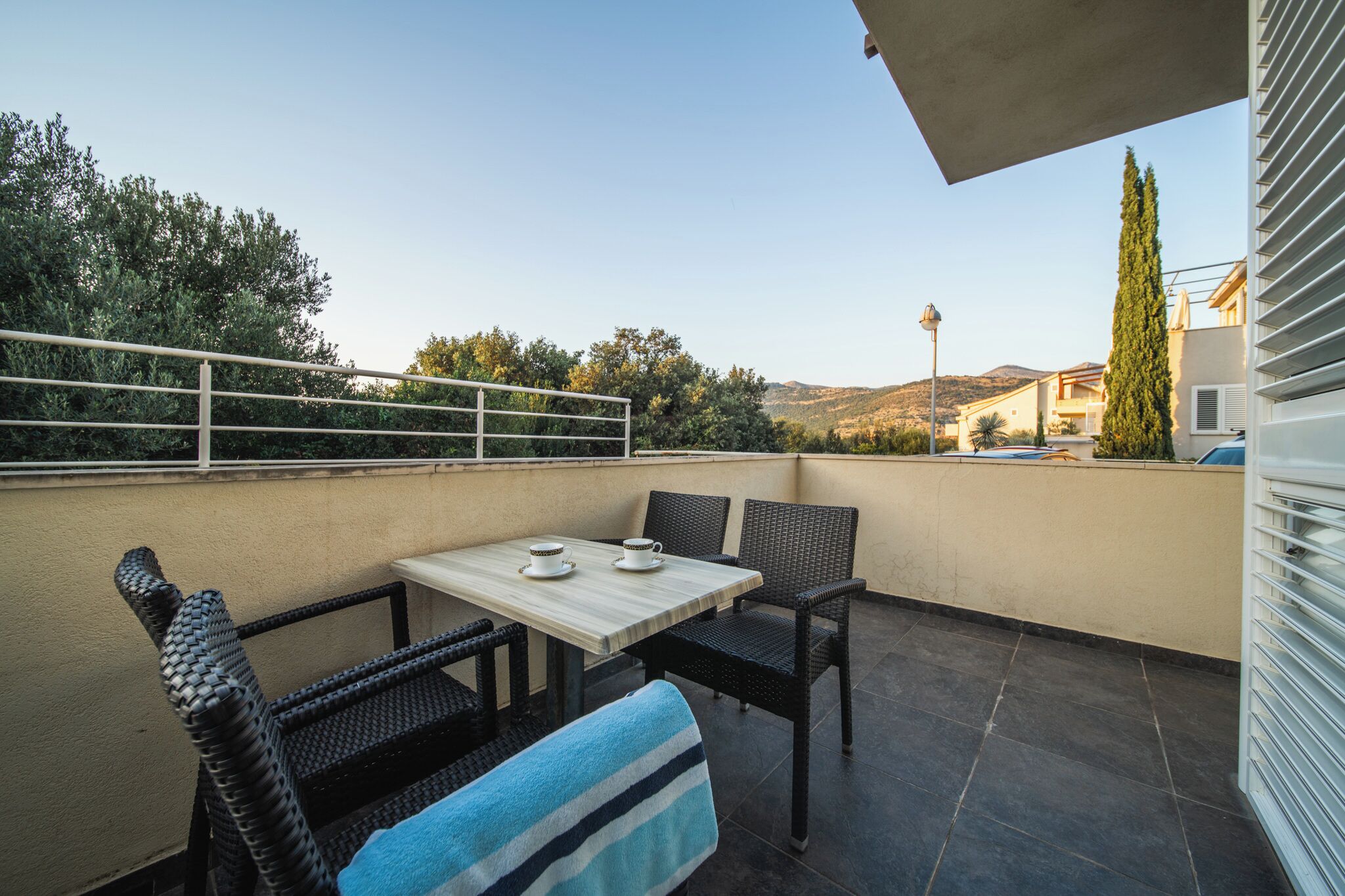 A balcony with a table and chairs, a view of the surrounding landscape, and a building in the background.