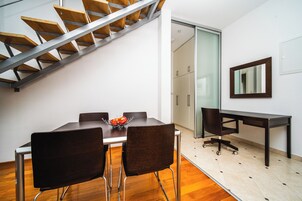Un comedor moderno con una escalera de madera, una mesa de comedor con sillas, un aparador de vidrio y un escritorio con una silla.