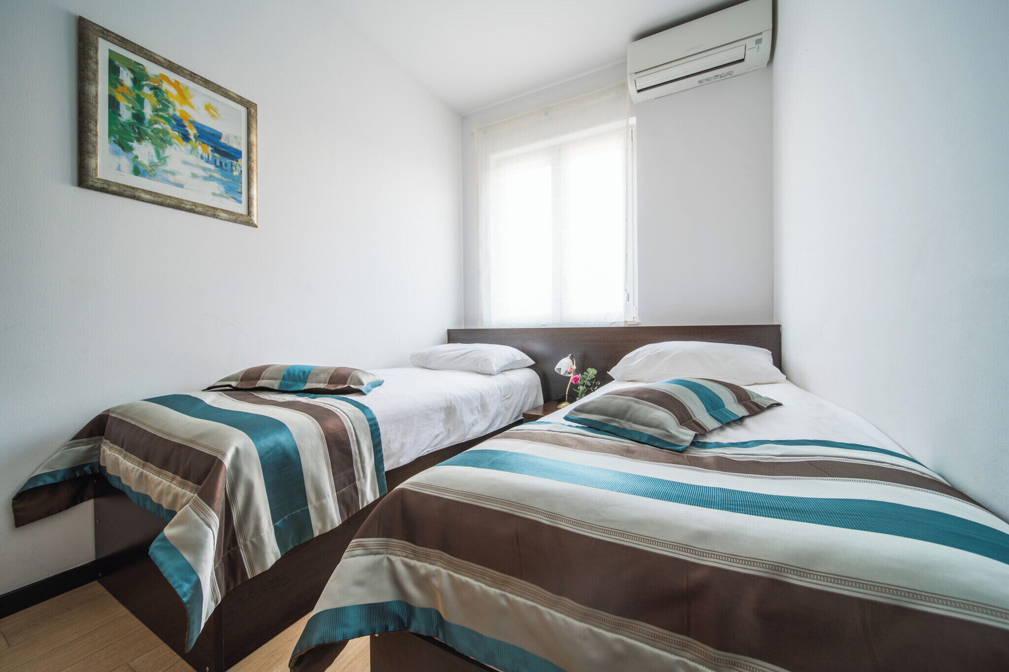 A hotel room with two beds, a painting on the wall, and an air conditioning unit.