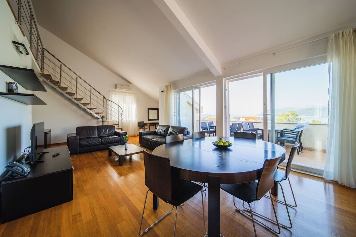 Un vaste espace de vie comprenant une grande table ronde, des canapés en cuir et un escalier menant à un niveau supérieur.