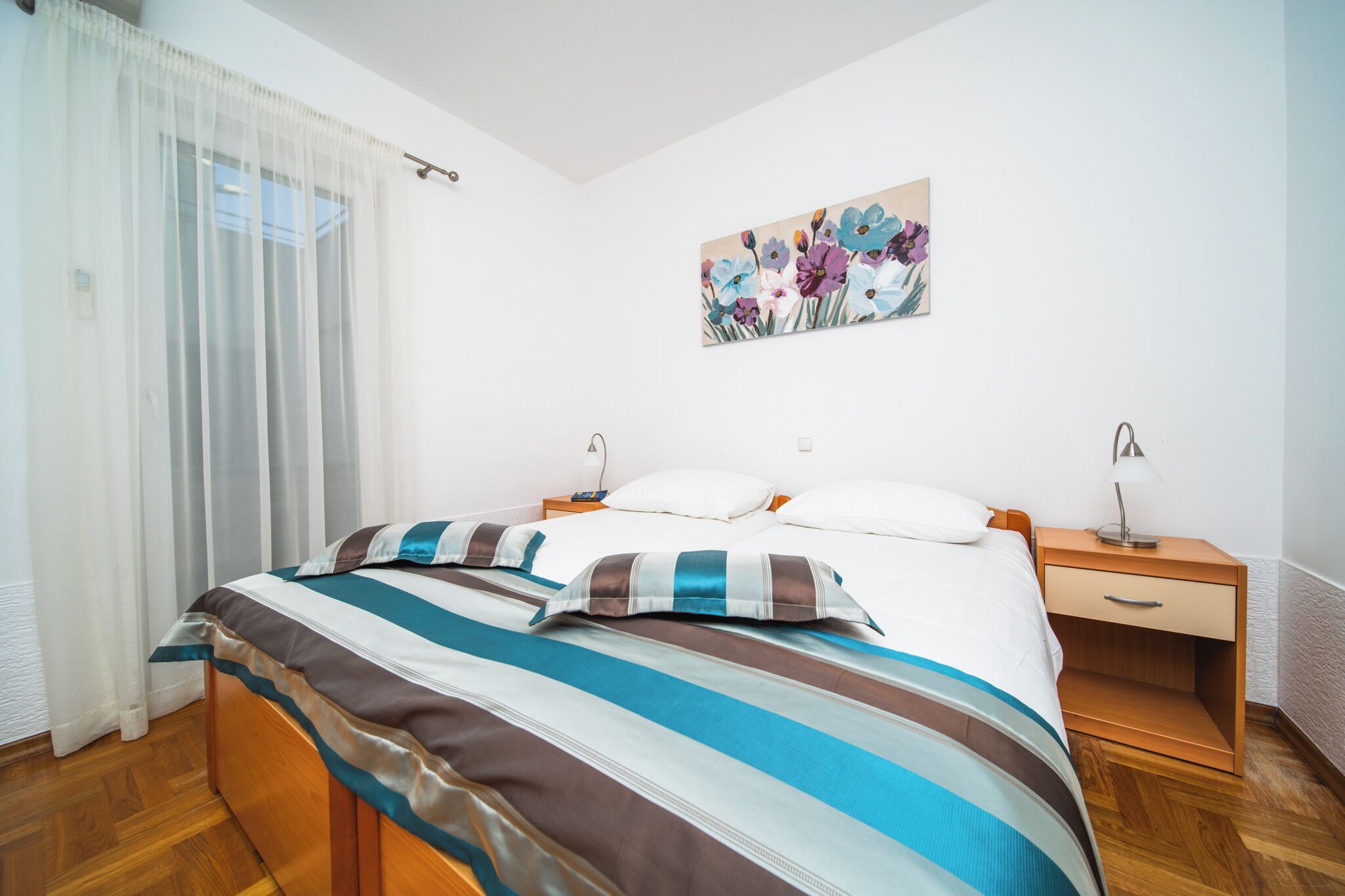 Quarto com cama, mesa de cabeceira, abajur e pintura floral na parede.