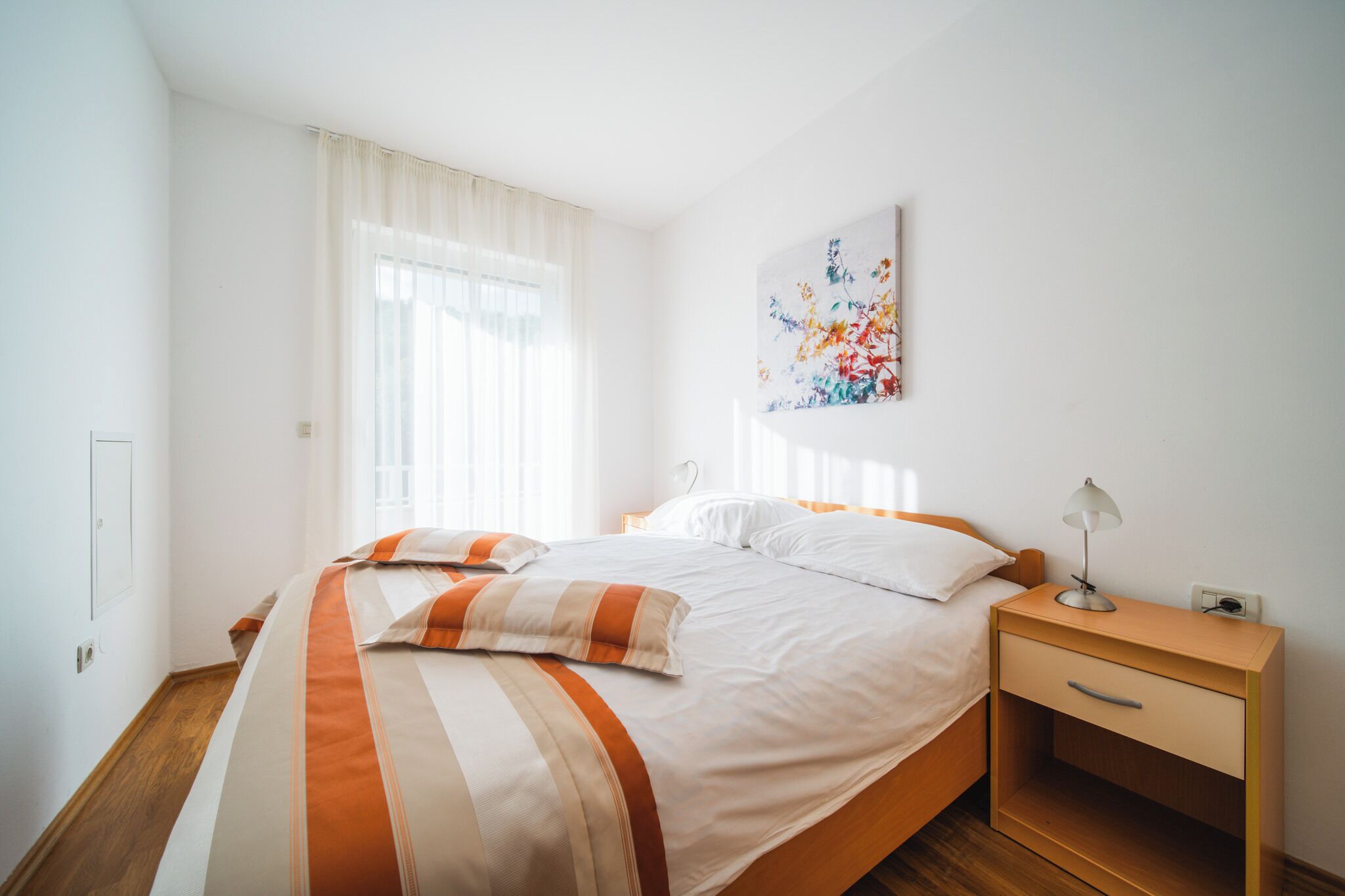 A neatly arranged bedroom with a bed, bedside table, and a wall-mounted artwork.