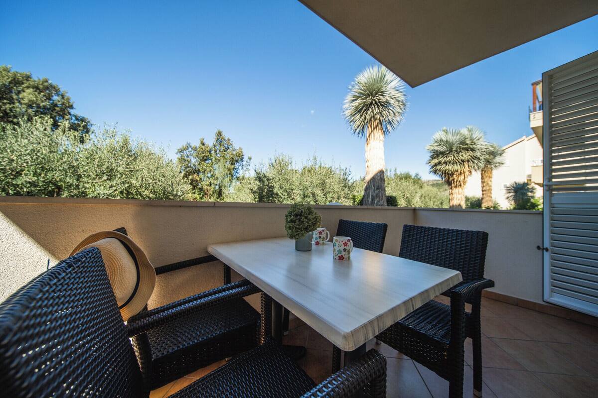 Une terrasse extérieure avec une table et des chaises en osier, entourée de verdure et sous un ciel dégagé.