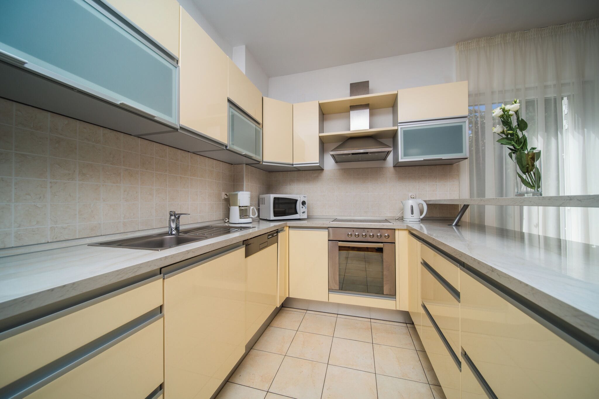 A modern kitchen with beige cabinets, a microwave, a coffee maker, and a dishwasher.