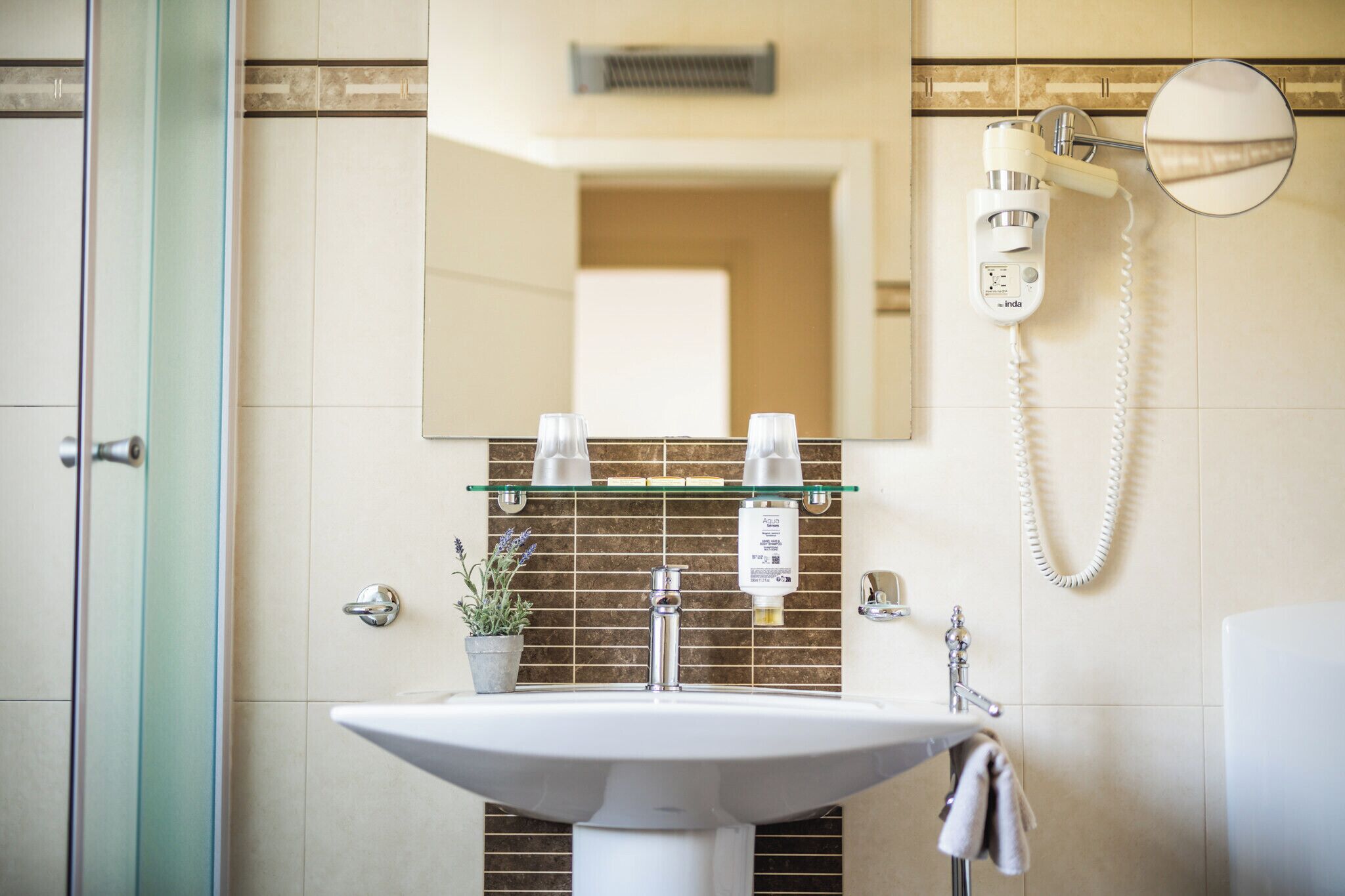 A bathroom with a white sink, a glass shelf with toiletries, a hairdryer, and a mirror.