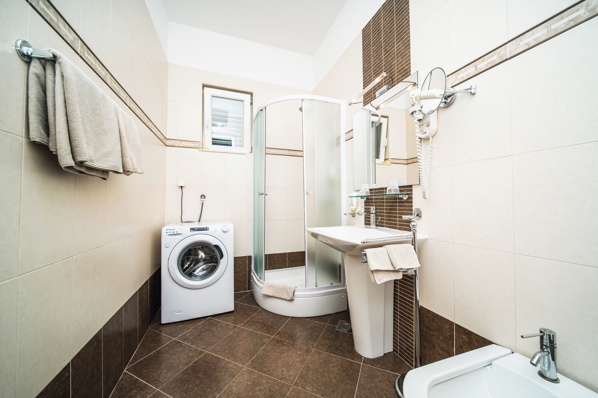 A compact bathroom with a washing machine, a glass-enclosed shower, a sink, and a mirror.