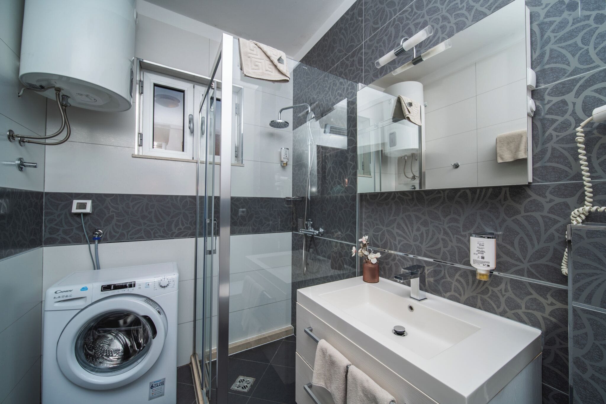A modern bathroom with a glass-enclosed shower, a built-in washing machine, and a large mirror above the sink.