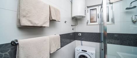Un baño moderno con lavadora, un perchero con dos toallas, una ducha con puerta de vidrio y un inodoro.