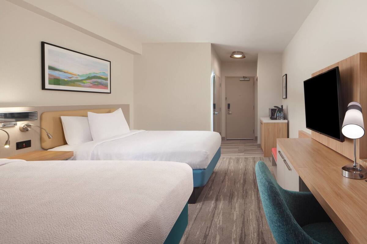 Une chambre d’hôtel avec deux lits, une télévision, un bureau et une salle de bain visible à travers une porte.